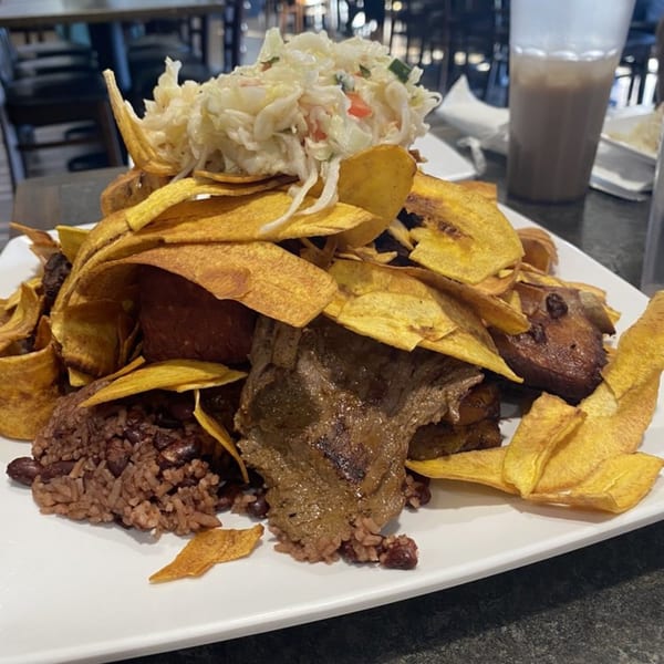 A large plate of Salvadoran food with fried plantain chips, beef, rice, beans, and curtido.