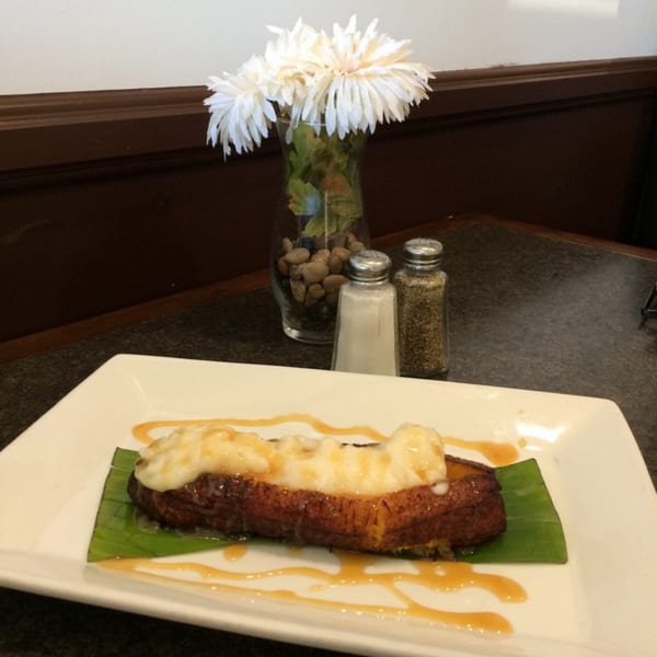Fried plantain topped with cream and caramel drizzle, served on a white plate with a banana leaf.
