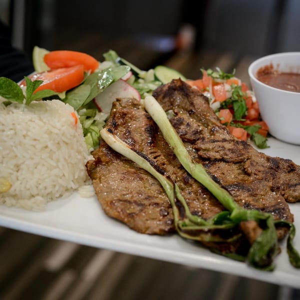 Grilled steak with green onions, white rice, fresh salad, pico de gallo, and a side of beans.