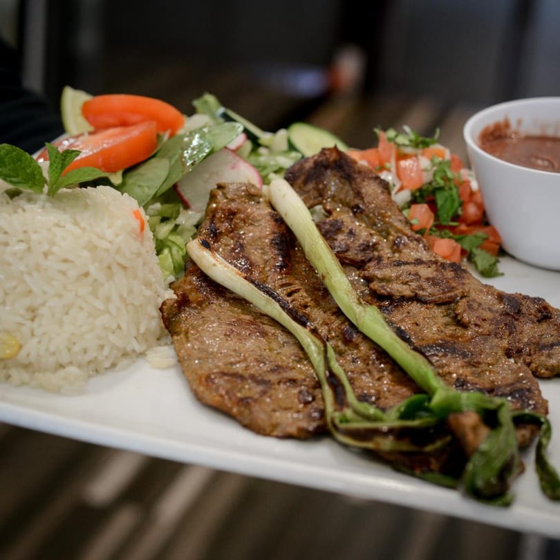 Grilled steak with green onions, white rice, fresh salad, pico de gallo, and a side of beans.