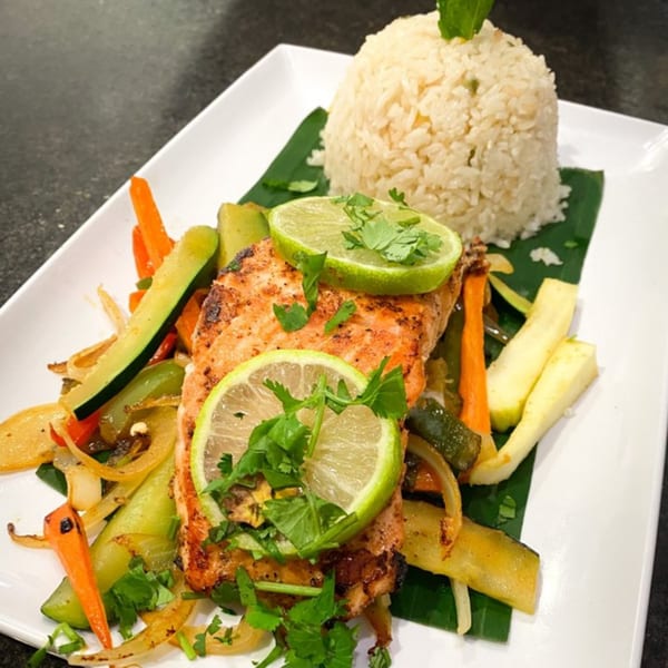 Grilled salmon with lime, cilantro, and sautéed vegetables, served with rice on a banana leaf.